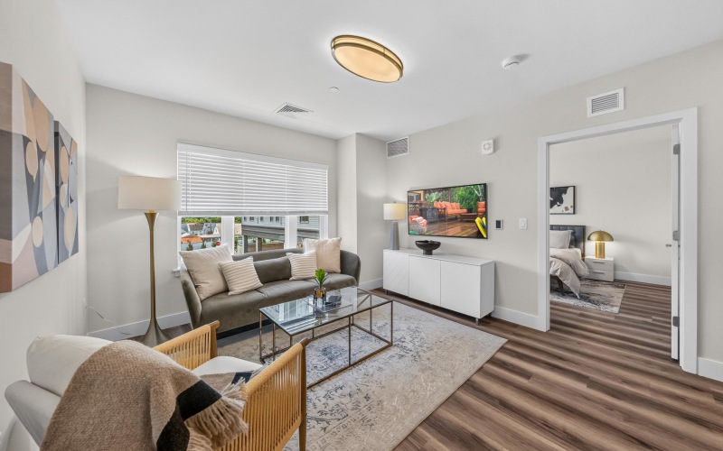 Apartment living space with seating and TV, looking into bedroom